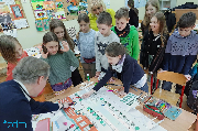 Grupa dzieci stoi wokół stołu, na którym jest mapa ulicy i przybory piśmiennicze.