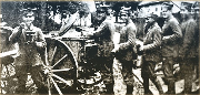 Grupa uśmiechniętych powstańców stoi przy kuchni polowej.